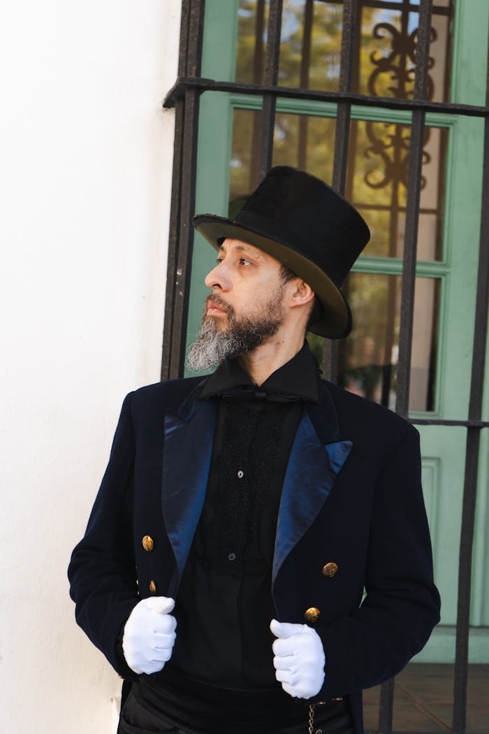 about-us Elegant man in Victorian attire with top hat and gloves, gazing thoughtfully outdoors.